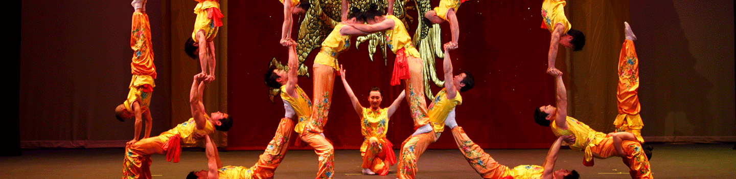 Acrobats form a human pyramid in gold and orange costumes.